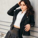 A woman in a skirt and leather jacket leaning against a wall